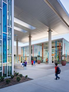 people are walking around in front of a building with glass walls and columns on both sides