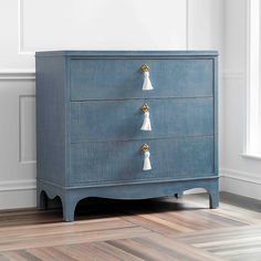 a blue dresser with three white tassels on the top and two gold handles