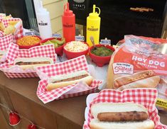 hotdogs and other condiments are on the table with red checkered napkins