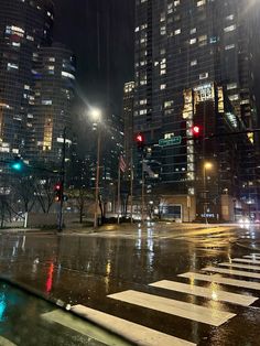 an intersection in the city at night with traffic lights and street signs on wet pavement