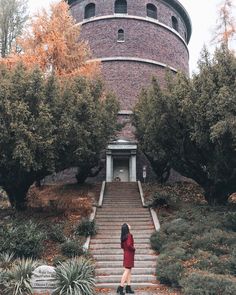 a woman in a red dress is walking up stairs to a round building with trees