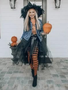 a woman dressed up as a witch holding two pumpkins