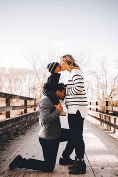 a man kneeling down next to a woman on a wooden bridge with trees in the background