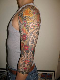 a man with a fish tattoo on his arm and shoulder is standing in front of a white wall