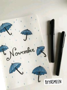 an open notebook with blue umbrellas and the words november written on it next to a pen