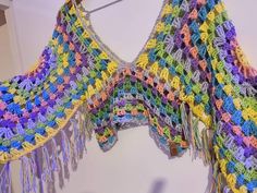 a multicolored crocheted shawl hanging from a hook on a wall