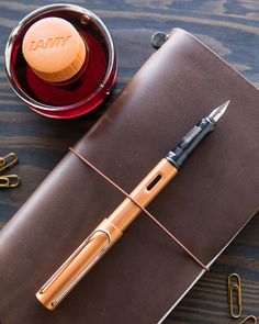 a brown leather notebook with a pen and paper clip next to it on a wooden table