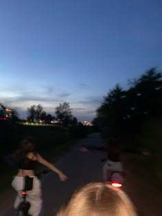 two people riding bikes down a road at night time with the sun setting behind them