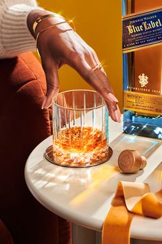 a woman is holding onto a glass with some liquor in it on a table next to a bottle