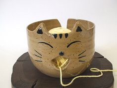 a ceramic cat head on top of a piece of wood with a yellow string attached to it