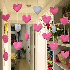 pink and white heart shaped balloons hanging from the ceiling in a hallway with shelves on either side