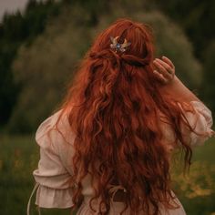 a woman with long red hair standing in a field