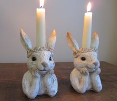 two white rabbits sitting next to each other with candles in front of them on a table