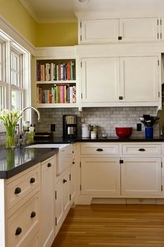 a kitchen with white cabinets and black counter tops in front of an open bookcase