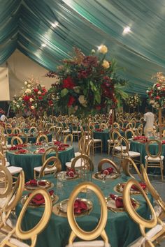 a banquet hall with tables and chairs covered in green tablecloths, red flowers and greenery