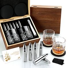 an assortment of liquor glasses and bottles in a wooden box next to two shot glasses