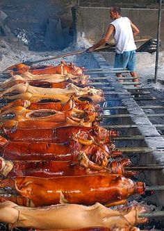 the man is grilling several large meats on an outdoor grill with tongs