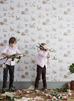 two young boys holding scissors in front of a wall with dinosaurs on the wallpaper