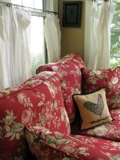 a red couch sitting in front of a window covered in white drapes and pillows