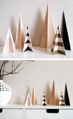 several wooden christmas trees on a shelf next to a white vase and black and white wall