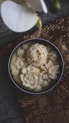 a bowl filled with flowers sitting on top of a wooden table next to a white flower