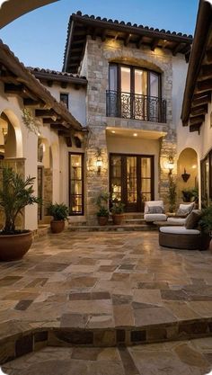 an outdoor patio with seating and potted plants in front of a house at dusk