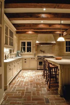 a kitchen with brick flooring and white cabinets, an island in the middle is surrounded by bar stools