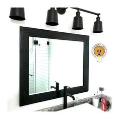 a bathroom mirror sitting above a sink under three black light fixture lights and a wall mounted faucet