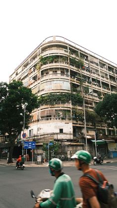 two people on scooters in front of a building with plants growing out of it