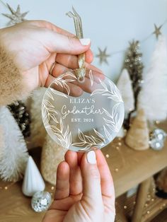 two hands holding a personalized glass ornament in front of christmas tree decorations