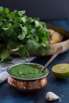 a copper bowl filled with green sauce next to some cilantro and limes