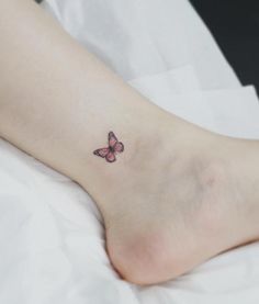 a small pink butterfly tattoo on the left side of the foot, sitting on top of a white sheet