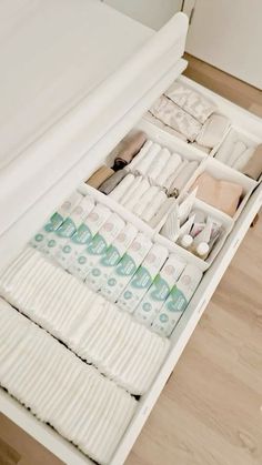 an open drawer filled with lots of items on top of a wooden floor next to a bed