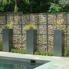 an outdoor swimming pool with stone walls and plants on each side, surrounded by grass