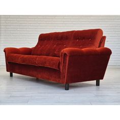 a red couch sitting on top of a hard wood floor next to a white brick wall