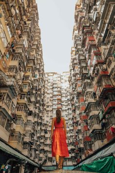 a woman in an orange dress standing on the edge of a building with many balconies