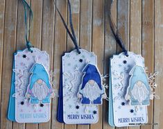 three tags with christmas gnomes and snowflakes hanging on a wooden table top