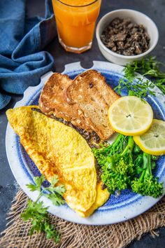 an omelet with broccoli, lemon and mushrooms on a plate next to a glass of orange juice