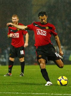 two men are playing soccer on a field in the rain while one man is about to kick the ball