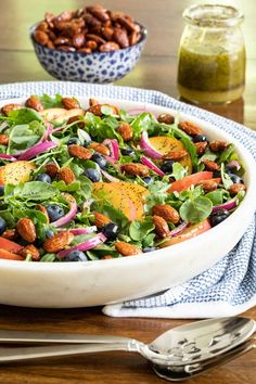 a white bowl filled with salad and nuts on top of a table next to silverware