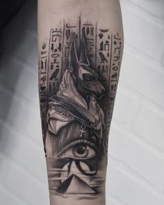 an egyptian tattoo on the leg with eye and pyramids in black and grey colors