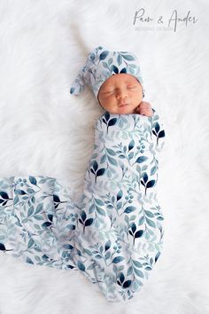 a newborn baby wrapped in a blue and white leaf print swaddled to it's side