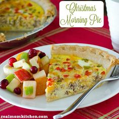 a white plate topped with a slice of quiche next to a bowl of fruit