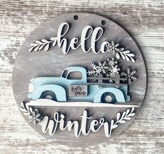 a metal sign that says hello winter with an old blue truck and snowflakes