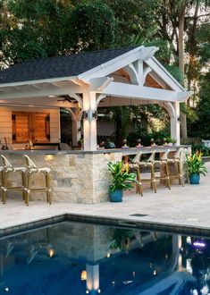 an outdoor bar with chairs around it next to a swimming pool and gazebo in the background