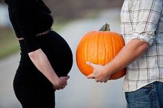 a pregnant woman holding a pumpkin in front of a man's belly as he stands next to her