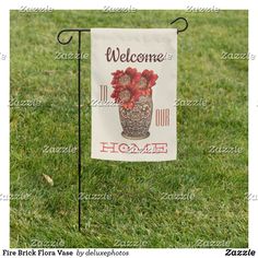 a welcome home sign in the grass with red flowers and potted plants on it