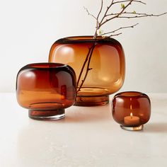 three brown vases sitting next to each other on a white counter top with a twig in it