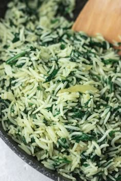 a pan filled with rice and spinach next to a wooden spoon