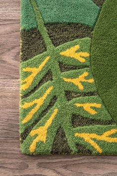 a green and yellow area rug on top of a wooden floor next to a plant